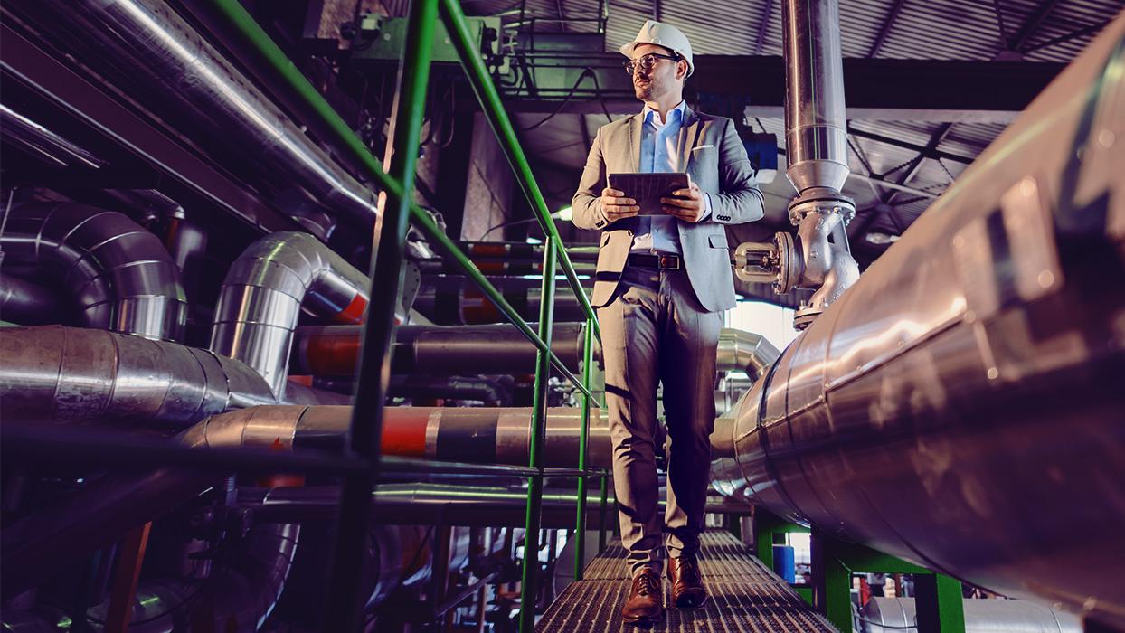 Man in suit walks through factory building with tablet